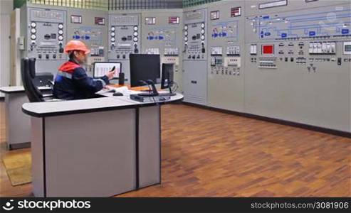 engineer sits and talks on phone at main control panel of gas compressor station