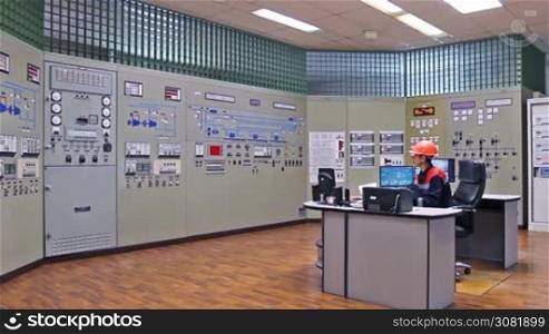 engineer sits at table on main control panel of gas compressor station, wide angle
