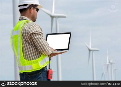 Engineer standing and playing laptop with wind turbine.
