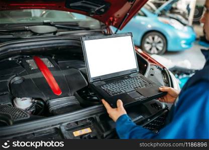 Engineer with laptop makes computer diagnostics of the car engine in auto-service. Vehicle wiring inspection. Engineer makes computer diagnostics of car engine