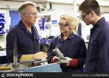 Engineer Working With Apprentices On Factory Floor