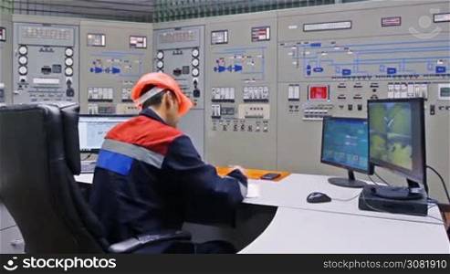 engineer writes down log while looking into monitors with schema, surveillance cameras near main control panel of gas compressor station, closeup