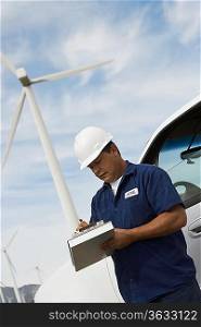 Engineer writing on clipboard by car at wind farm