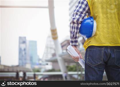 Engineering and construction concept. Closeup engineer with blue. Engineering and construction concept. Closeup engineer with blueprint and helmet standing on site, blurred high building in city, with free copy space.