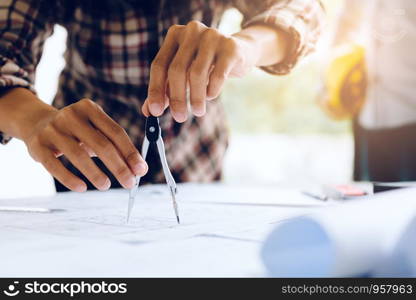 Engineering man working on blueprint in workplace and drawing compass.