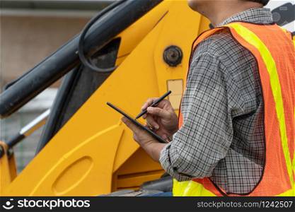 Engineering wearing a white safety helmet standing in front of the backhoe Looking at home construction work And use the tablet to check the blueprint with construction