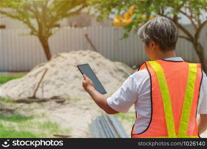 Engineering wearing a white safety helmet standing In front of the construction site And using tablet to construction. Concepts for controlling and checking the construction accuracy