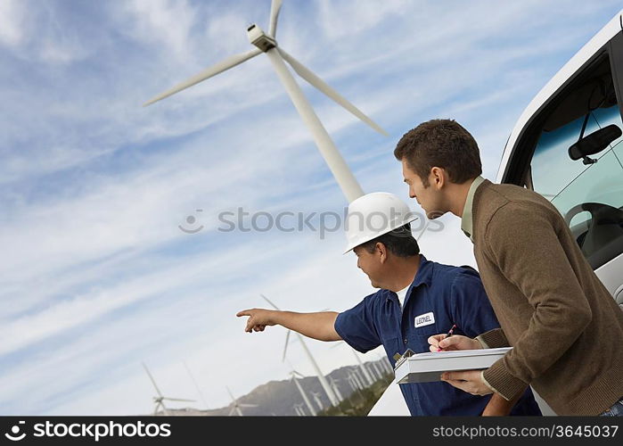 Engineers examining wind turbines by car at wind farm