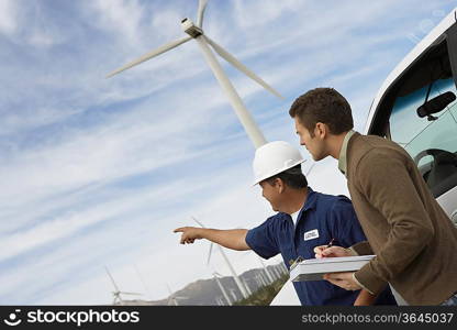 Engineers examining wind turbines by car at wind farm
