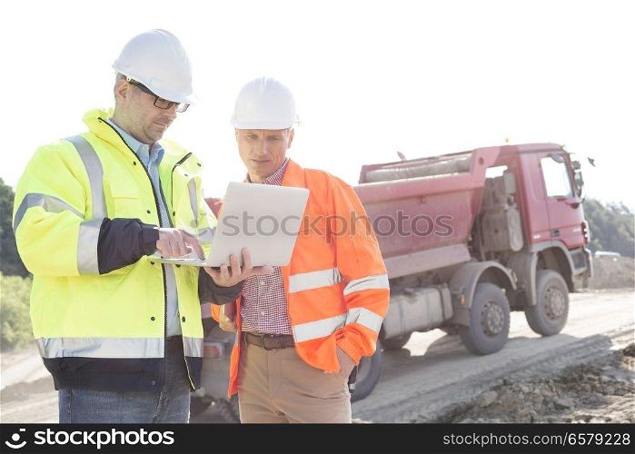 Engineers using laptop at construction site against clear sky on sunny day