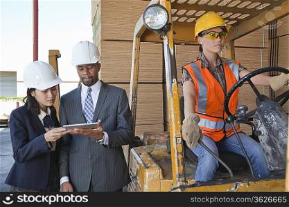 Engineers using tablet PC with female industrial worker driving forklift truck