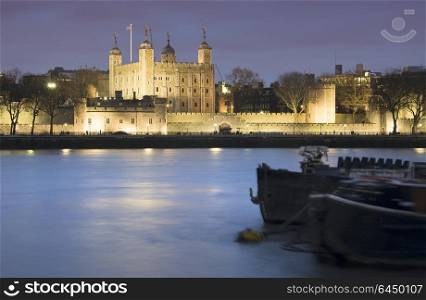 England, London, Tower of London. Tower of London at night with river barges.. Tower of London at night with river barges in foreground
