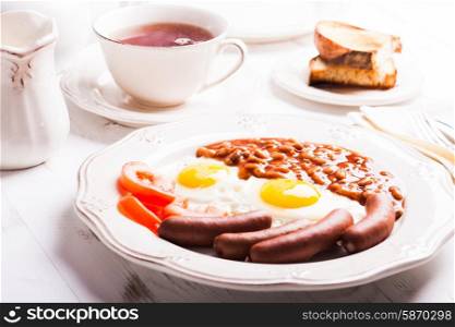 English breakfast - eggs, sausages with beans and tea with milk