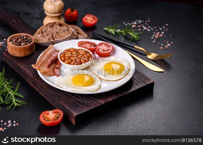 English breakfast with fried eggs, bacon, beans, tomatoes, spices and herbs. A hearty and nutritious start of the day. English breakfast with fried eggs, bacon, beans, tomatoes, spices and herbs
