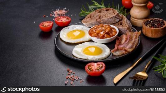 English breakfast with fried eggs, bacon, beans, tomatoes, spices and herbs. A hearty and nutritious start of the day. English breakfast with fried eggs, bacon, beans, tomatoes, spices and herbs