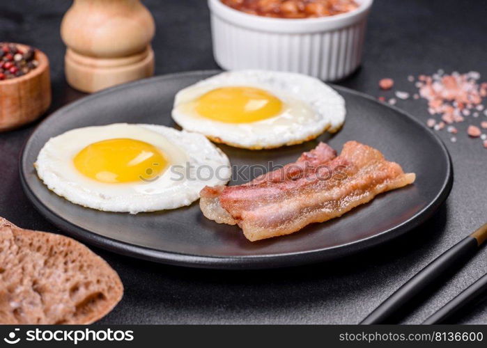 English breakfast with fried eggs, bacon, beans, tomatoes, spices and herbs. A hearty and nutritious start of the day. English breakfast with fried eggs, bacon, beans, tomatoes, spices and herbs