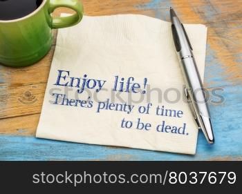 Enjoy life! There is plenty of time to be dead. Handwriting on a napkin with a cup of coffee,