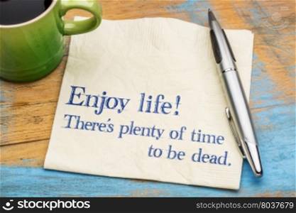 Enjoy life! There is plenty of time to be dead. Handwriting on a napkin with a cup of coffee,