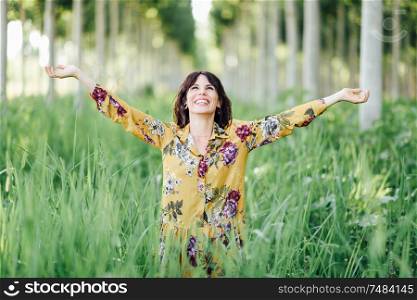 Enjoying the nature. Young woman arms raised enjoying the fresh air in green forest. Female wearing flowered dress.. Woman arms raised enjoying the fresh air in green forest