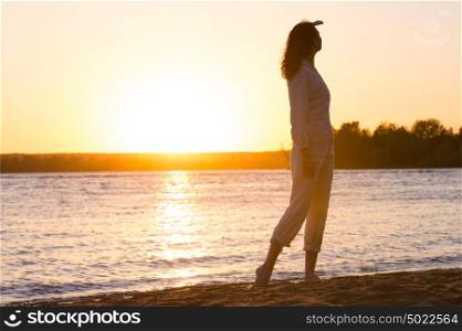 Enjoyment - free happy woman enjoying sunset. Beautiful woman in natural white shirt looking to the golden sunshine glow of sunset with arm near face enjoying peace, serenity in nature