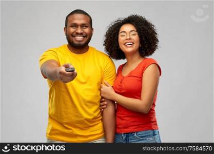entertainment and people concept - happy african american couple with tv remote control over grey background. african american couple with tv remote control