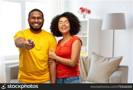 entertainment and people concept - happy african american couple with tv remote control over home background. african american couple with tv remote control