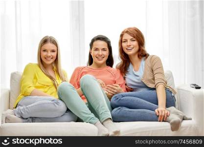 entertainment, leisure and friendship concept - three smiling teenage girls or friends with popcorn watching tv at home. teenage girls or friends watching tv at home