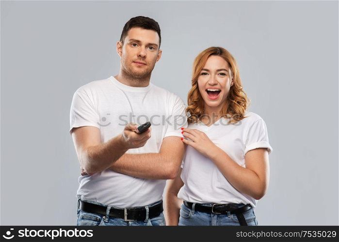 entertainment, television and people concept - couple in white t-shirts with tv remote control over grey background. couple with tv remote control