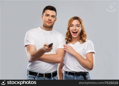 entertainment, television and people concept - couple in white t-shirts with tv remote control over grey background. couple with tv remote control