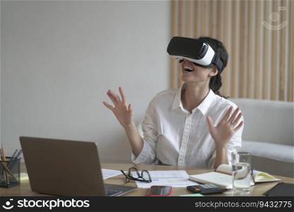 Enthusiastic business lady wears VR headset for laptop raising hands up as trying to touch objects in 3D reality when sitting at desk, working with apps online, modern technology for business concept. Business lady wears VR headset for laptop raising hands up as trying to touch objects in 3D reality