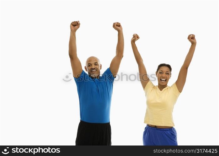 Enthusiastic mid adult multiethnic man and woman wearing exercise clothing with arms stretched overhead in excitement.
