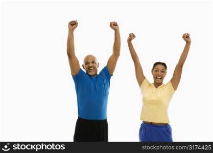 Enthusiastic mid adult multiethnic man and woman wearing exercise clothing with arms stretched overhead in excitement.