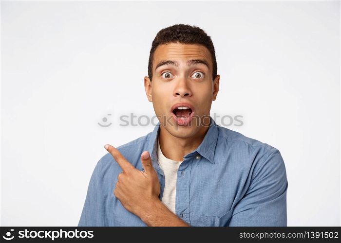 Enthusiastic, surprised hispanic man in blue shirt over t-shirt, pointing upper left corner, gasping and drop jaw amazed, popping eyes camera, impressed with new product, look astonished.. Enthusiastic, surprised hispanic man in blue shirt over t-shirt, pointing upper left corner, gasping and drop jaw amazed, popping eyes camera, impressed with new product, look astonished