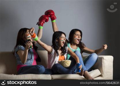 Enthusiastic young female friends screaming out while watching boxing match together at home