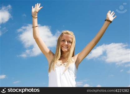 Enthusiastic young teen girl raising her arms in celebration against a blue sky.