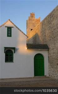 Entrance of a traditional house near the fortification wall and tower in twilight in the medina of Asilah, Morocco