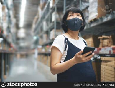 Entrepreneur, Female business Owner in protective face mask holding smartphone in warehouse store while her pregnancy. Young Asian Pregnant Woman buyer using phone and looking at shelf at mall