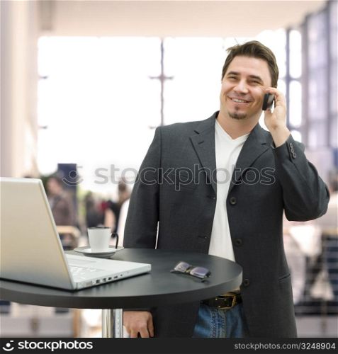 Entrepreneur standing by coffee table and calling on mobile phone.