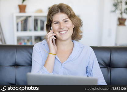 Entrepreneur woman wearing blue shirt working with a laptop sitting on a couch at home