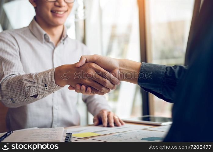 Entrepreneurs collaboration deal shaking hands in a modern office and financial paper graph on desk.