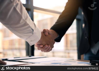 Entrepreneurs collaboration deal shaking hands in a modern office and financial paper graph on desk.