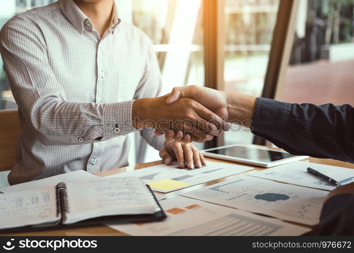 Entrepreneurs collaboration deal shaking hands in a modern office and financial paper graph on desk.