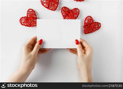 Envelope with a letter in hands on a white background. Blank card in hands on a white background - concept for design. Congratulatory letter on the background of hearts for Valentine&rsquo;s Day.. Envelope with a letter in hands on a white background