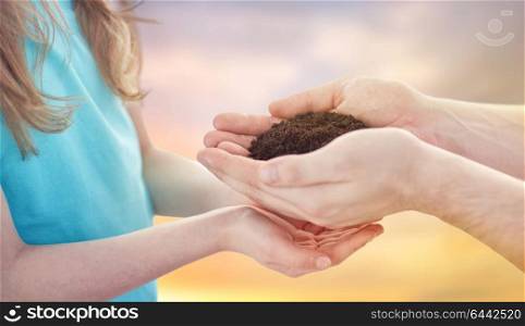 environment, family and legacy concept - close up of father and daughter holding soil in cupped hands over sky background. close up of father and daughter hands holding soil