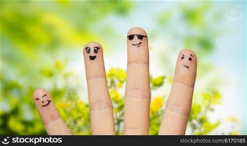 environment, family, summer holidays, people and body parts concept - close up of four fingers with smiley faces over natural green herbal background