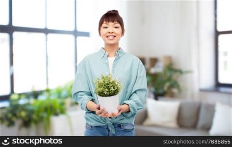 environment, nature and people concept - happy smiling asian woman holding flower in pot over home background. happy smiling asian woman holding flower in pot