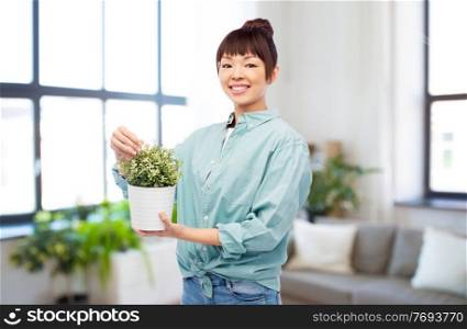 environment, nature and people concept - happy smiling asian woman holding flower in pot over home room background. happy smiling asian woman holding flower in pot