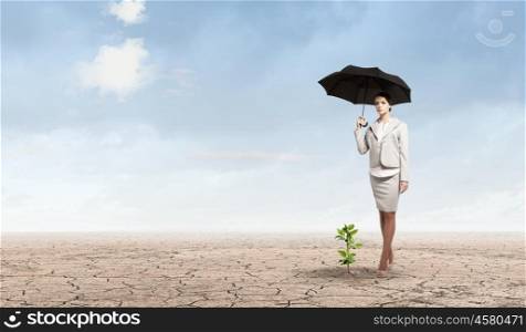 Environment protection. Attractive businesswoman protecting green sprout with umbrella