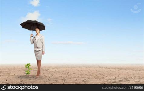 Environment protection. Attractive businesswoman protecting green sprout with umbrella