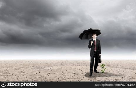 Environment protection. Young businessman protecting little sprout with umbrella